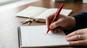 Hands with red pen marking late rent date on calendar. 
